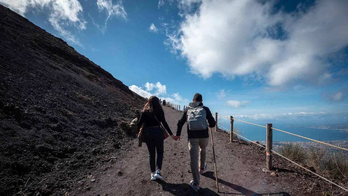 Walkers on the cinder path around the Mount Vesuvius crater with the Bay of Naples hazy below, the climb on the Pompeii and Vesuvius guided tour with lunch from Sorrento, Campania, Italy