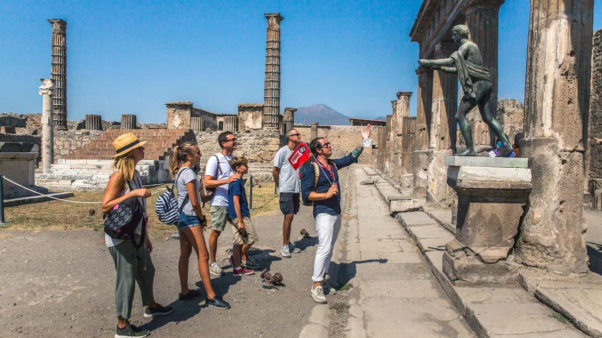 A guided group in the Forum of Pompeii with the flat summit of Vesuvius behind, the morning of the full-day Pompeii and Mount Vesuvius tour from Naples or Sorrento, Campania, Italy